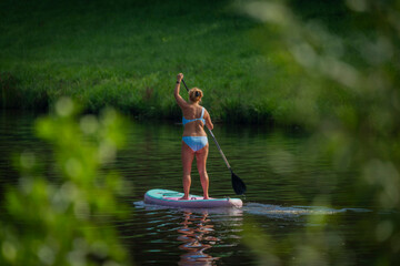 Paddle board with woman in blue swimsuit on Vltava river