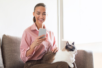 Happy Woman With Cat On Lap Texting Via Phone Indoor