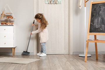 Cute little girl sweeping floor with broom at home