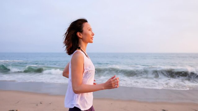 Attractive Asian woman jogging on the beach at sunset. Slow Motion.