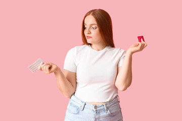 Young woman with condom and contraceptive pills on pink background