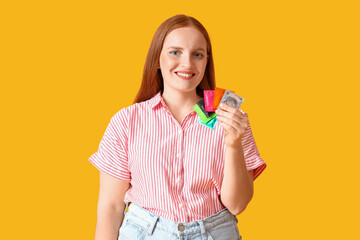 Young woman with condoms on yellow background