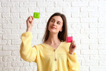 Young woman with condoms on white brick background