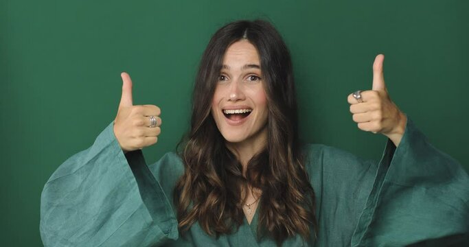 Young woman in green dress making good-bad sign isolated on green background. Girl make choice, or makes a decision thumb up or thumb down, like or dislike, yes or no. Girl diced thumbs up.