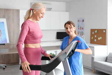 Female physiotherapist working with mature woman on treadmill in rehabilitation center