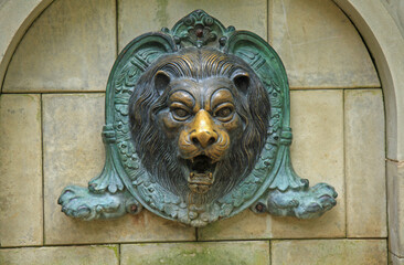 Bronze lion head. Mascaron, bas-relief, high relief of an animal in architecture. Decorative element of the fountain made of metal. Sculpture in garden and park architecture. Lion in park improvement