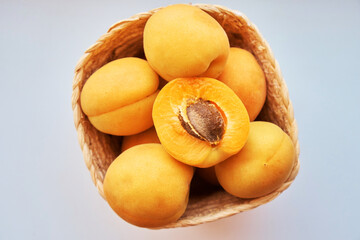 Half of an apricot lies among other apricots in a wicker basket on a white background. View from above. Up close