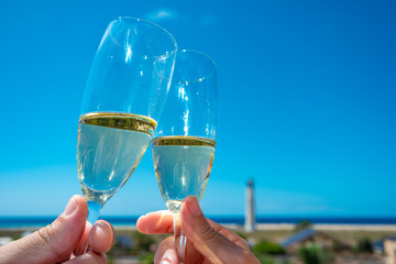 Amor y celebración con copas,  brindis de una pareja en playa o islas en verano bajo el sol con faro a lo lejos.