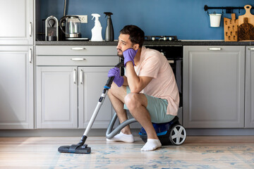 Tired and bored man in the kitchen feeling bad after cleaning house. Exhausted household concept	