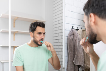 Handsome man brushing teeth and looking at the mirror in the bathroom	