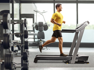 Obraz na płótnie Canvas Profile shot of a young man running on a treadmill at a gym