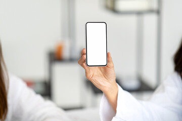 European adult lady doctor nutritionist in white coat recommends app on phone with blank screen to patient