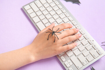 Female hand with modern computer keyboard and spider for Halloween on purple background, closeup