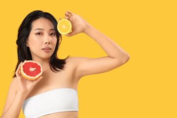 Beautiful young Asian woman with citrus fruits on yellow background