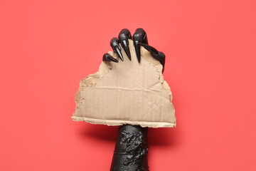 Black hand of witch with blank paper sheet on red background. Halloween celebration