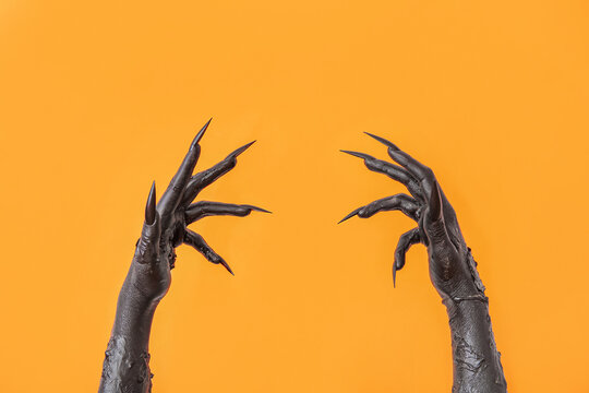 Black hands of witch on orange background. Halloween celebration