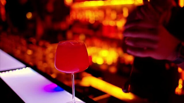 Barman making a cocktail with bitter alcohol at the bar at night with red neon lights, slow motion