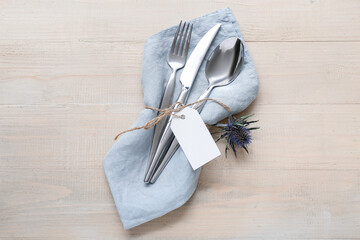 Silver cutlery with napkin on beige wooden background