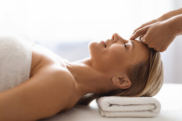 Peaceful middle aged woman getting healing head massage at modern luxury spa