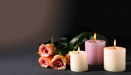 Burning candles and flowers on black background with space for text. Funeral concept