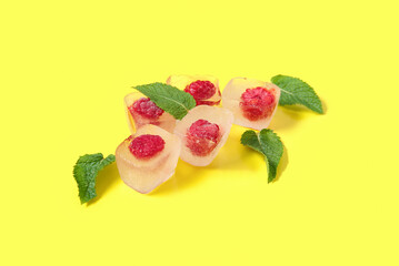 Frozen raspberries in ice cubes and mint on yellow background