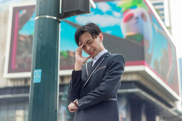 An irked and annoyed young asian man has a headache after a stressful situation. Outdoor city plaza...