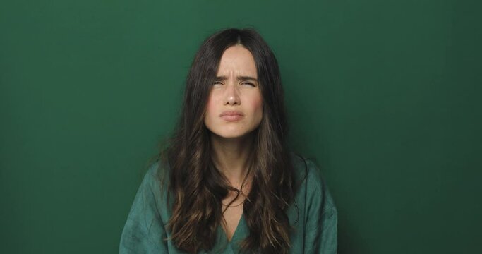 Brunette curly woman squinting trying to see or read text, running eyes standing isolated on green background. Problem with vision. 