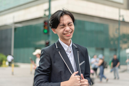 A hopeful and optimistic asian man in his early 20s chuckles while standing at the city plaza. A young ambitious employee.