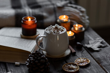 Aromatherapy on a grey fall morning, atmosphere of cosiness and relax. Autumn cozy home composition with hot chocolate with marshmallow and candles. Wooden background, books, close up.