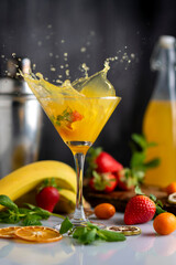 cocktail glass with fruit drink orange strawberries bananas and kumquats with mint leaves with liquid flying splash