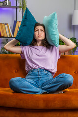 Repair work at neighbours. Irritated woman girl relaxing on couch cover ears with pillows annoyed...