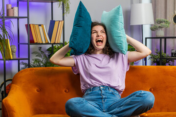 Repair work at neighbours. Irritated woman girl relaxing on couch cover ears with pillows annoyed...