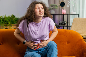Sick ill woman suffering from painful stomach ache, period cramps lying on sofa at home room. Girl...