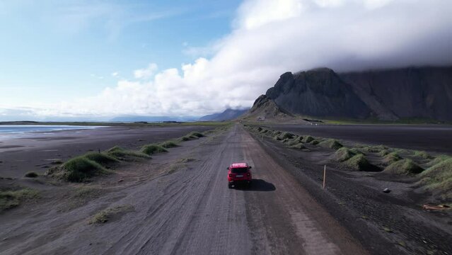 DRONE AERIAL FOOTAGE: Jeep 4X4 car driving the road with the Vestrahorn mountain and Stokksnes beach in the background. Vestrahorn Mountain is located in southeast Iceland near the town of H&ouml;fn.