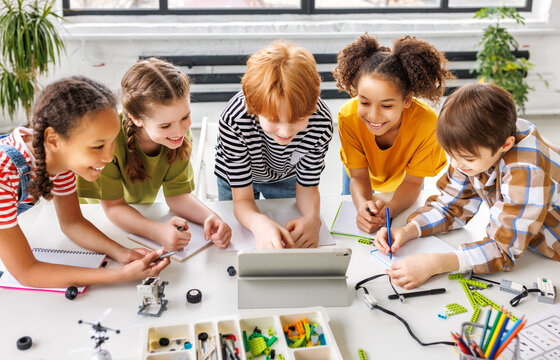 Cheerful  schoolkids   looking at tablet screen and study the scheme of assembly of robots during collective school work   during online lesson.