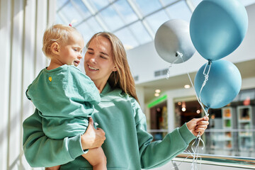 Portrait of happy mother with baby in her arms and colored balloons. Young pretty mom and her...