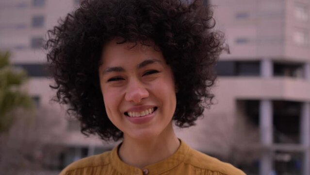 Close up of young adult African American woman looking happy at camera positive attitude. Real beautiful latina people smiling cheerful outdoors. Afro female posing laughing expression in city.