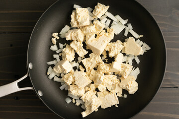 Crumbled Tofu and Onions Cooking in a Skillet: Large chunks of bean curd crumbles and diced onions in a nonstick frying pan