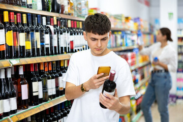 attentive buyer chooses bottle of wine for holiday. buyer man scan qr code from label