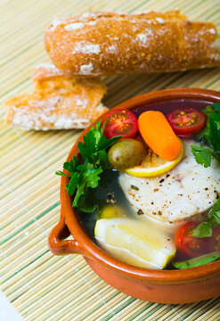 Fisher soup from merluccius. Recipe: boil broth from fish head, add potatoes, carrots, shallots, corn, fish fillets or steak 200 g, season with salt, pepper. Then cook in oven at 200 deg for 40min
