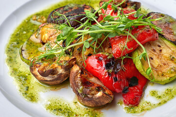 Grilled baked vegetables, eggplant, zucchini, bell pepper, champignon mushrooms, on a white plate against a dark background, with microgreen. close up