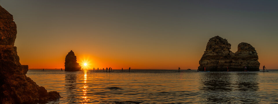 panoramic sunrise at coastal dream - praia do camilo, algarve portugal - standup paddling in the morning at sunrise