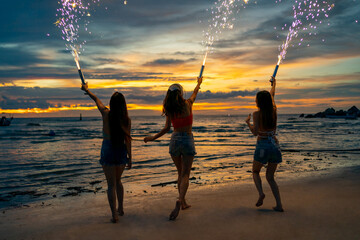 Group of Young Asian woman friends playing sparklers firework together at tropical island beach in summer night. Attractive girl enjoy and fun outdoor lifestyle beach party on holiday travel vacation.