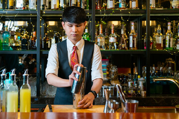 Professional Asian man bartender preparing and serving cocktail drink to customer on bar counter at nightclub. Barman making mixed alcoholic drink for celebrating holiday party at restaurant bar.