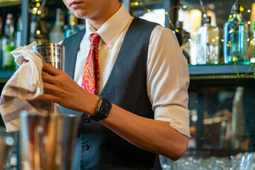 Professional Asian man bartender preparing and serving cocktail drink to customer on bar counter at nightclub. Barman making mixed alcoholic drink for celebrating holiday party at restaurant bar.