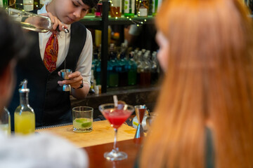 Professional Asian man bartender preparing and serving cocktail drink to customer on bar counter at nightclub. Barman making mixed alcoholic drink for celebrating holiday party at restaurant bar.
