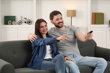 Happy couple watching show at home. Man changing TV channels with remote control