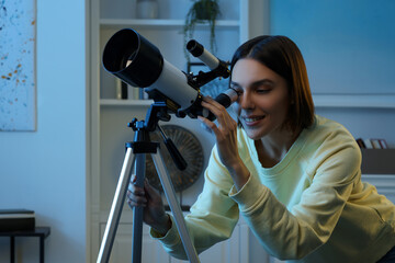 Beautiful young woman looking at stars through telescope in room