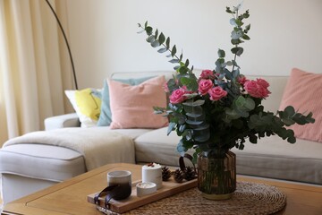 Beautiful bouquet of roses and eucalyptus branches in vase near candles on table at home. Space for text