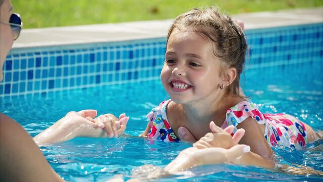Mother with father and daughter resting and swimming in a pool in summer, learning to swim